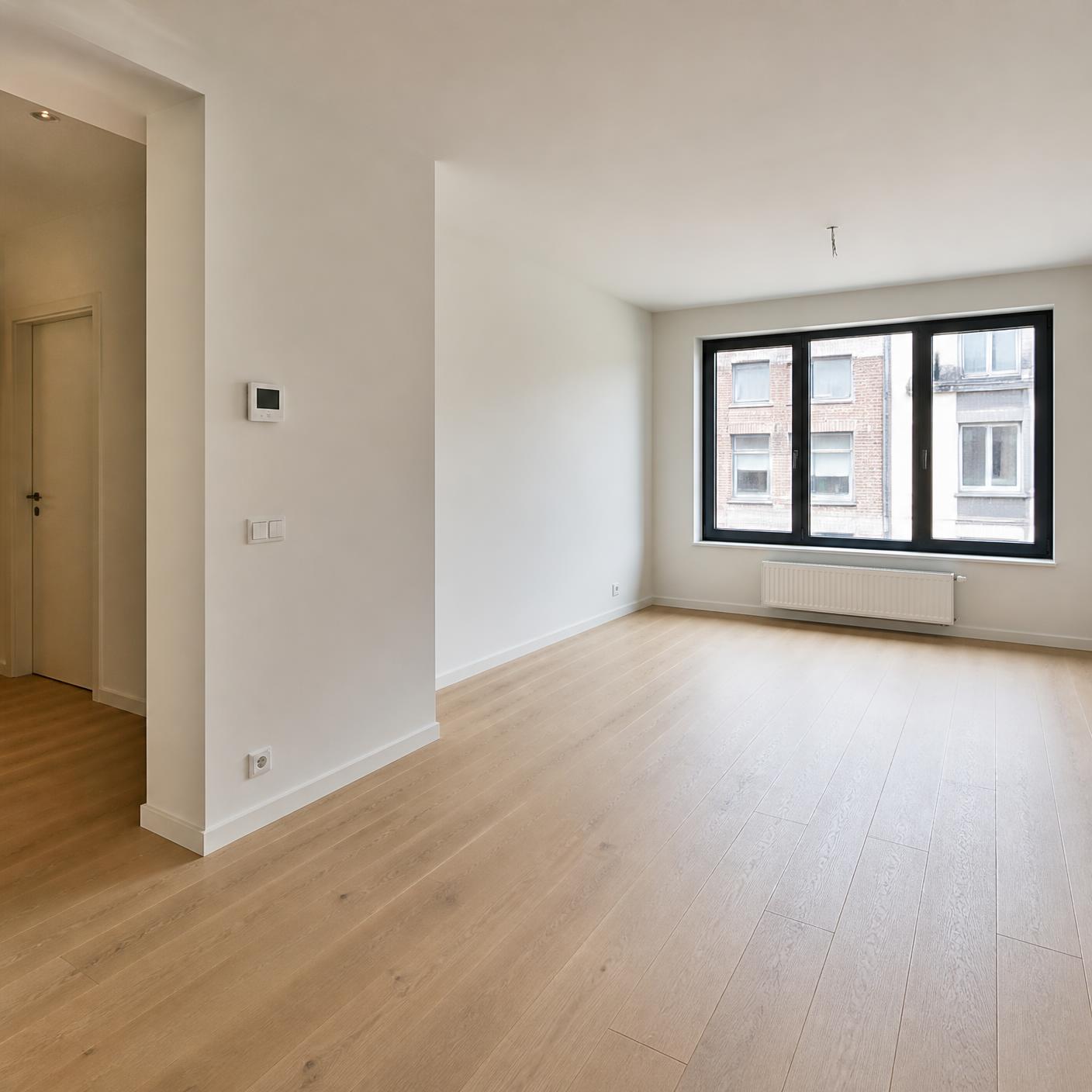 Lege, lichte woonkamer van een appartement met thermostaat aan de muur